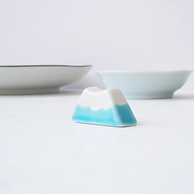 Gradient blue and white chopstick rest on a white surface with bowls in the background