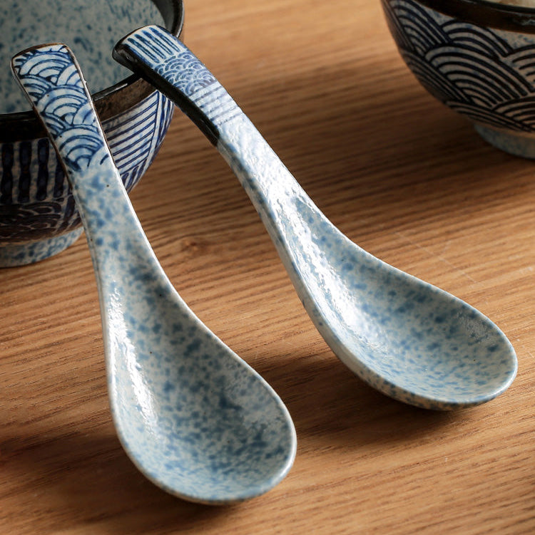 Two ceramic spoons with blue speckled pattern on a wooden surface.