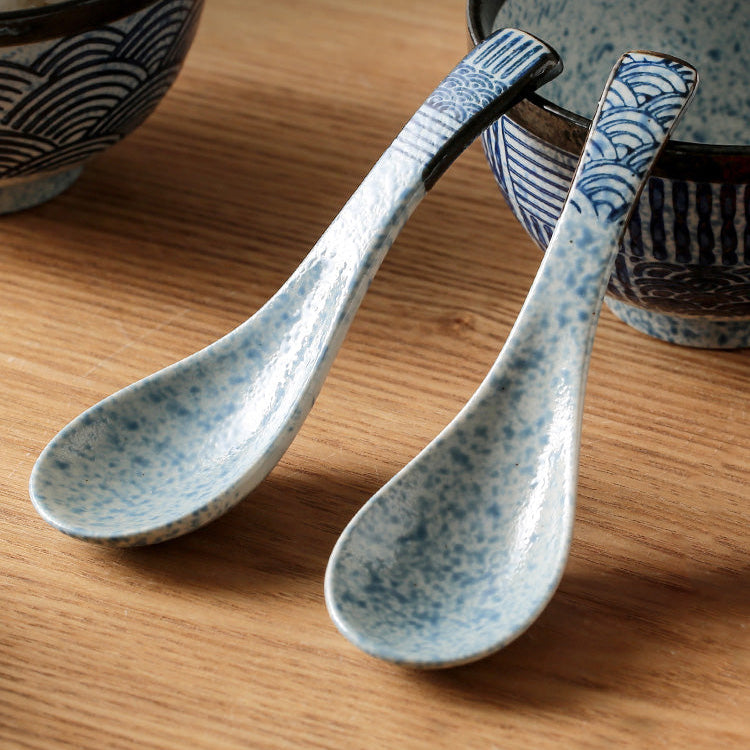 Two ceramic spoons on a wooden surface with Japanese text above them.