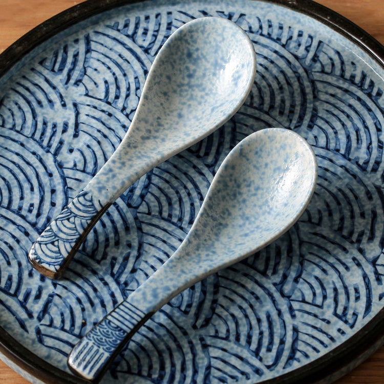 Two blue ceramic spoons on a matching plate with wave pattern on a wooden surface
