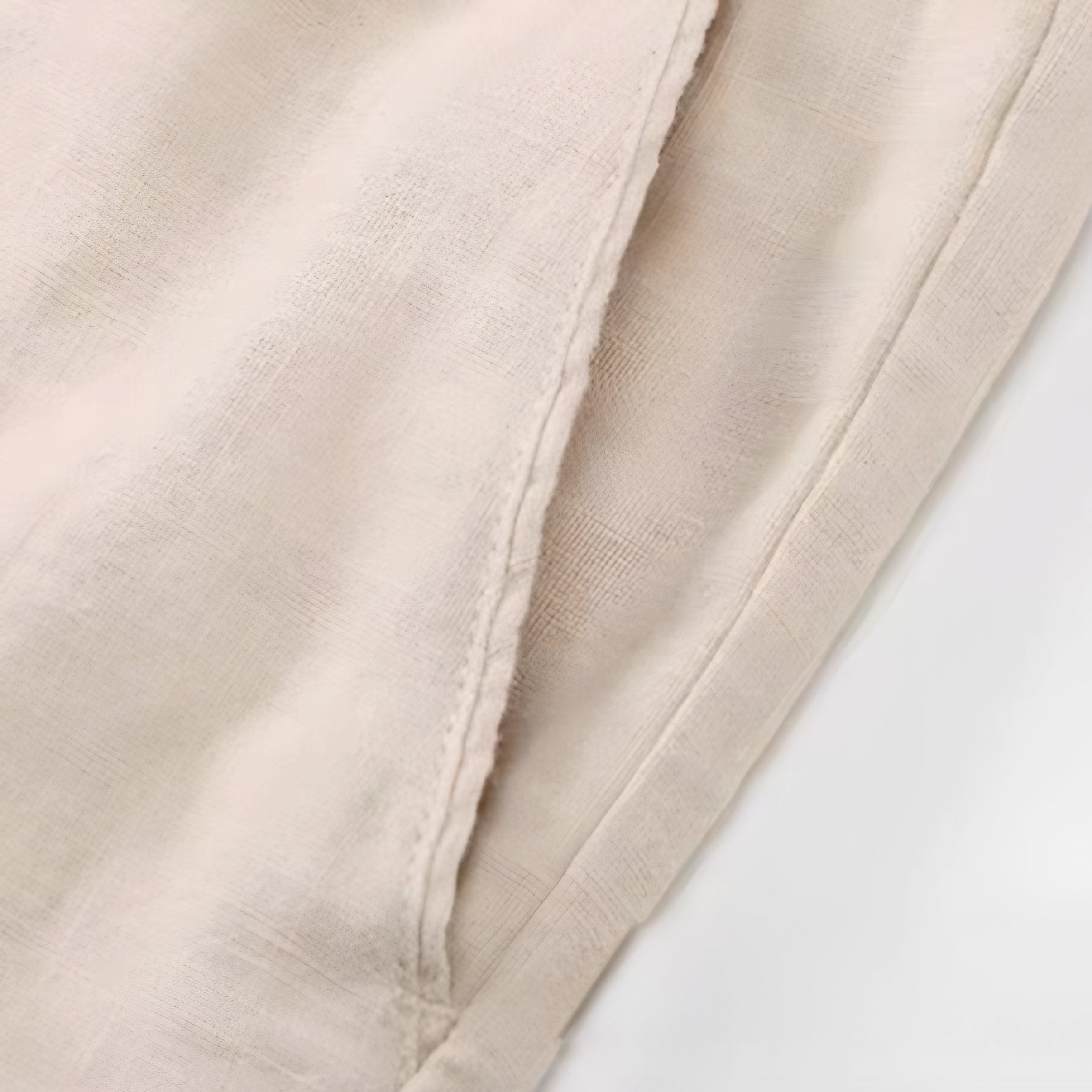 Close-up of a light beige fabric with a visible fold and stitched edge against a white background.