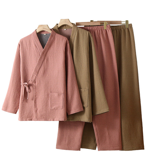 Two pairs of pants in pink and brown hanging on a rack against a white wall.