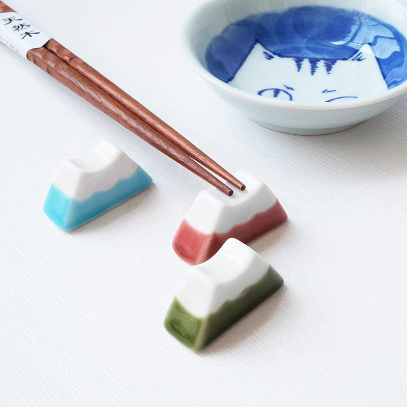 Three colorful chopstick rests with chopsticks and a bowl on a white surface