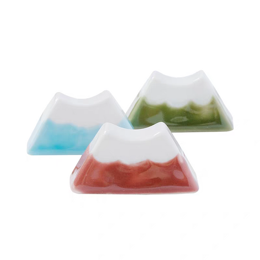 Three mountain-shaped ceramic chopstick rests with different colored bases on a white background
