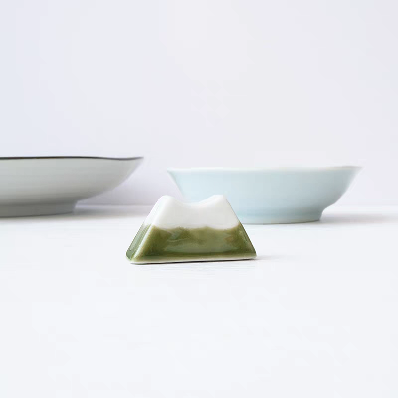 Pyramidal ceramic object with two bowls in the background on a light surface.