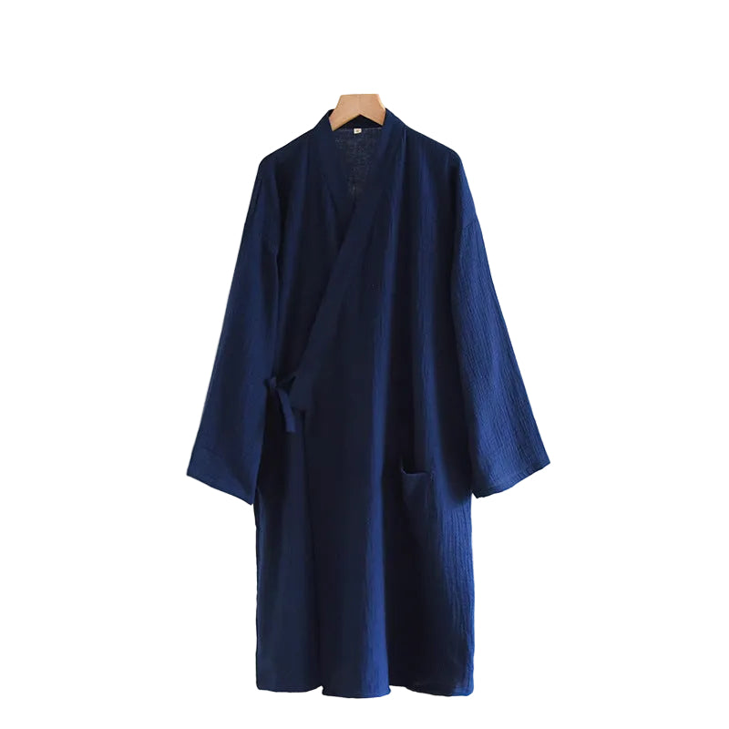 A dark navy blue textured kimono-style robe hanging on a wooden hanger against a white wall, with a small side table and books visible at the lower right.