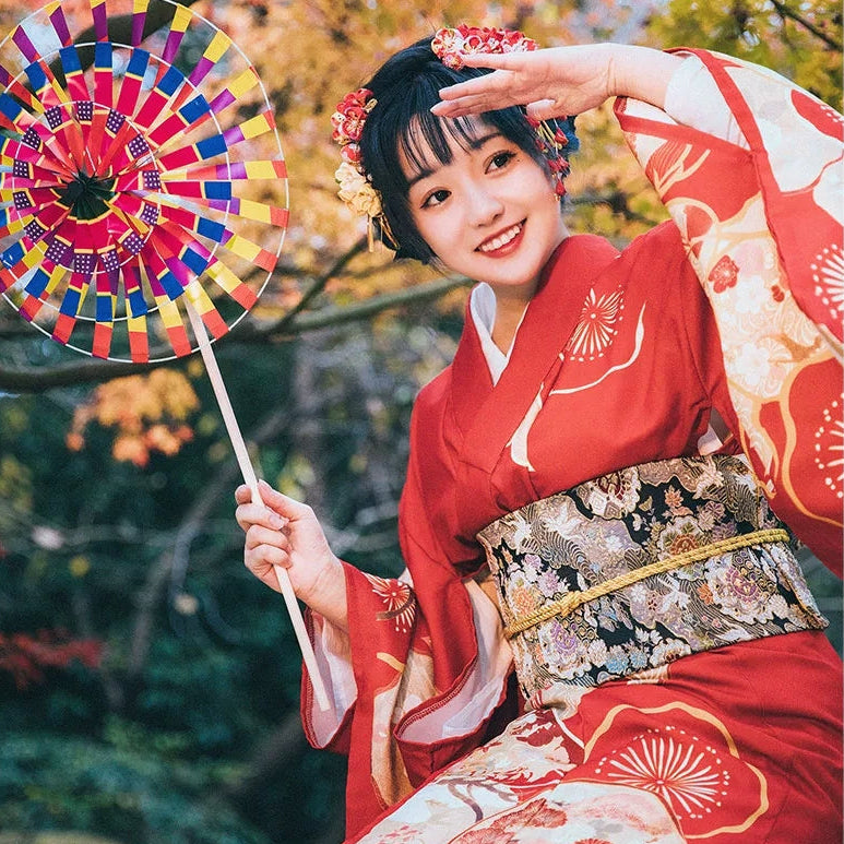 Woman in a red kimono holding a colorful fan with autumn foliage in the background