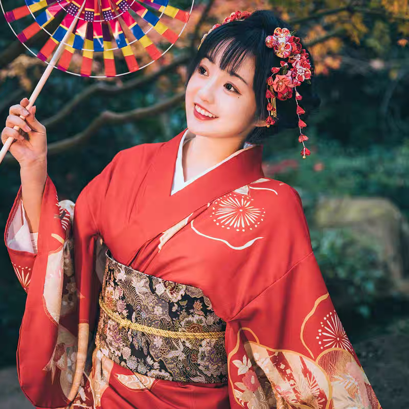 Woman in traditional red kimono with floral hair accessories and a colorful windmill in a natural setting.