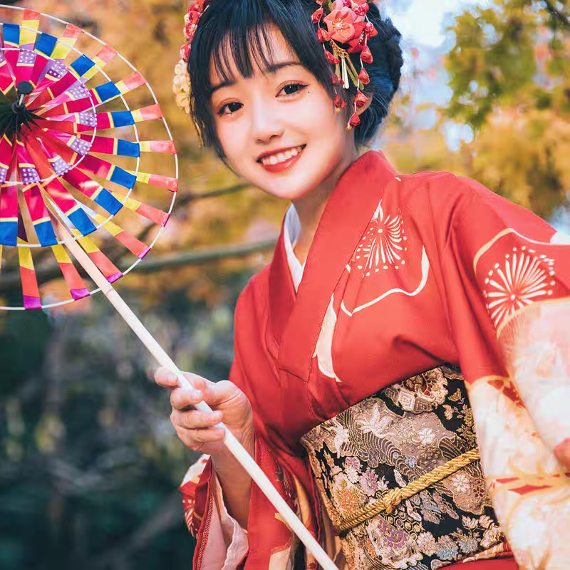 Woman in traditional red kimono with floral hair accessories and a colorful umbrella outdoors.