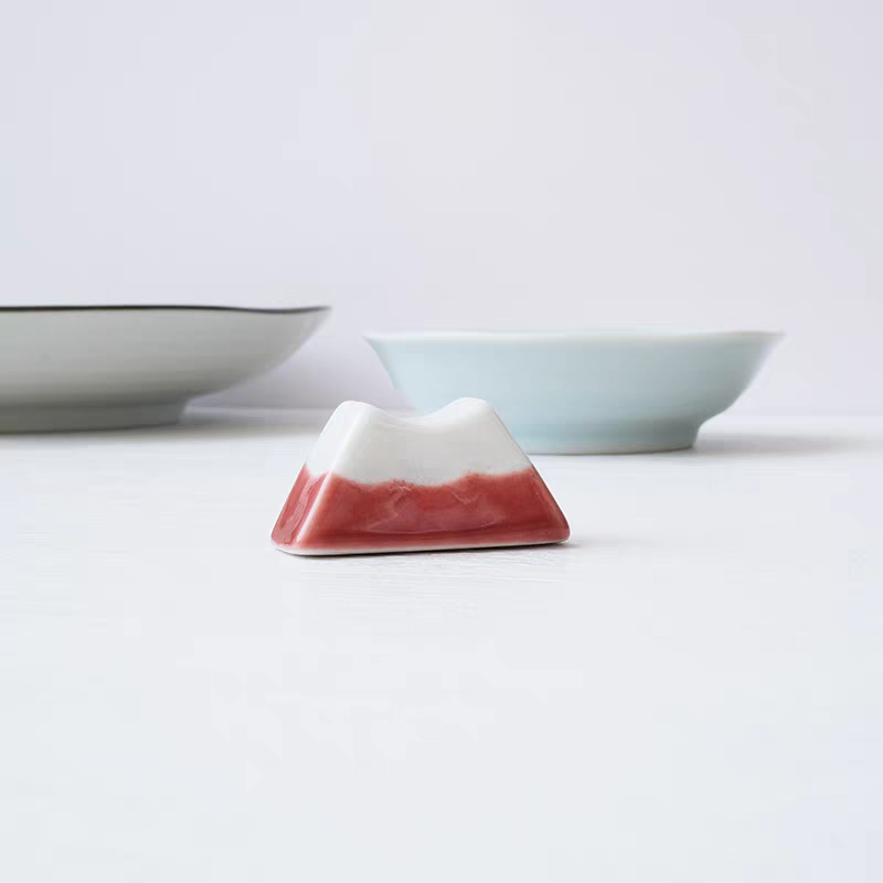 Ceramic mountain-shaped object with a white top and red base on a light gray background