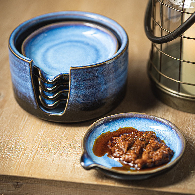 A set of blue and black glazed ceramic dipping bowls and a small serving dish filled with brown sauce, styled on a wooden surface next to a lantern.