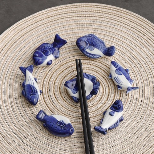 Blue and white fish-shaped ceramic items arranged on a woven mat with black chopsticks.