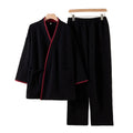 Black robe and pants set with red trim on hangers against a beige background