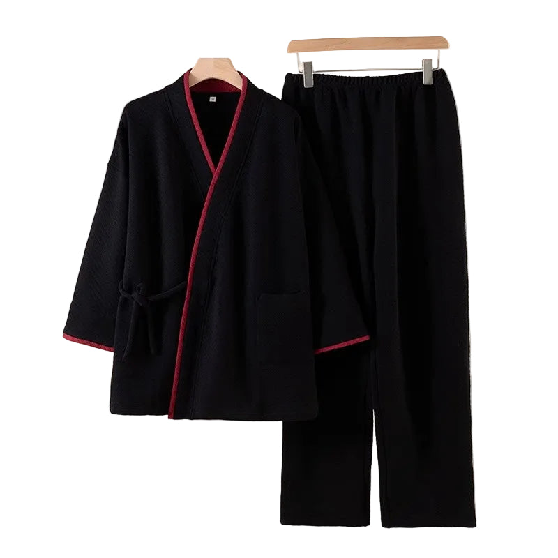 Black robe and pants set with red trim on hangers against a beige background