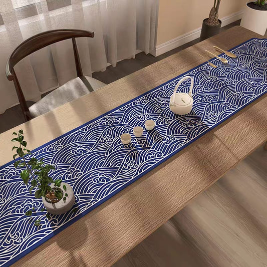 Table with a blue and white wave-patterned table runner, plants, and teacups.