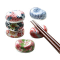 A set of multicolored, pebble-shaped Japanese ceramic chopstick rests with traditional Japanese patterns displayed alongside a pair of chopsticks.